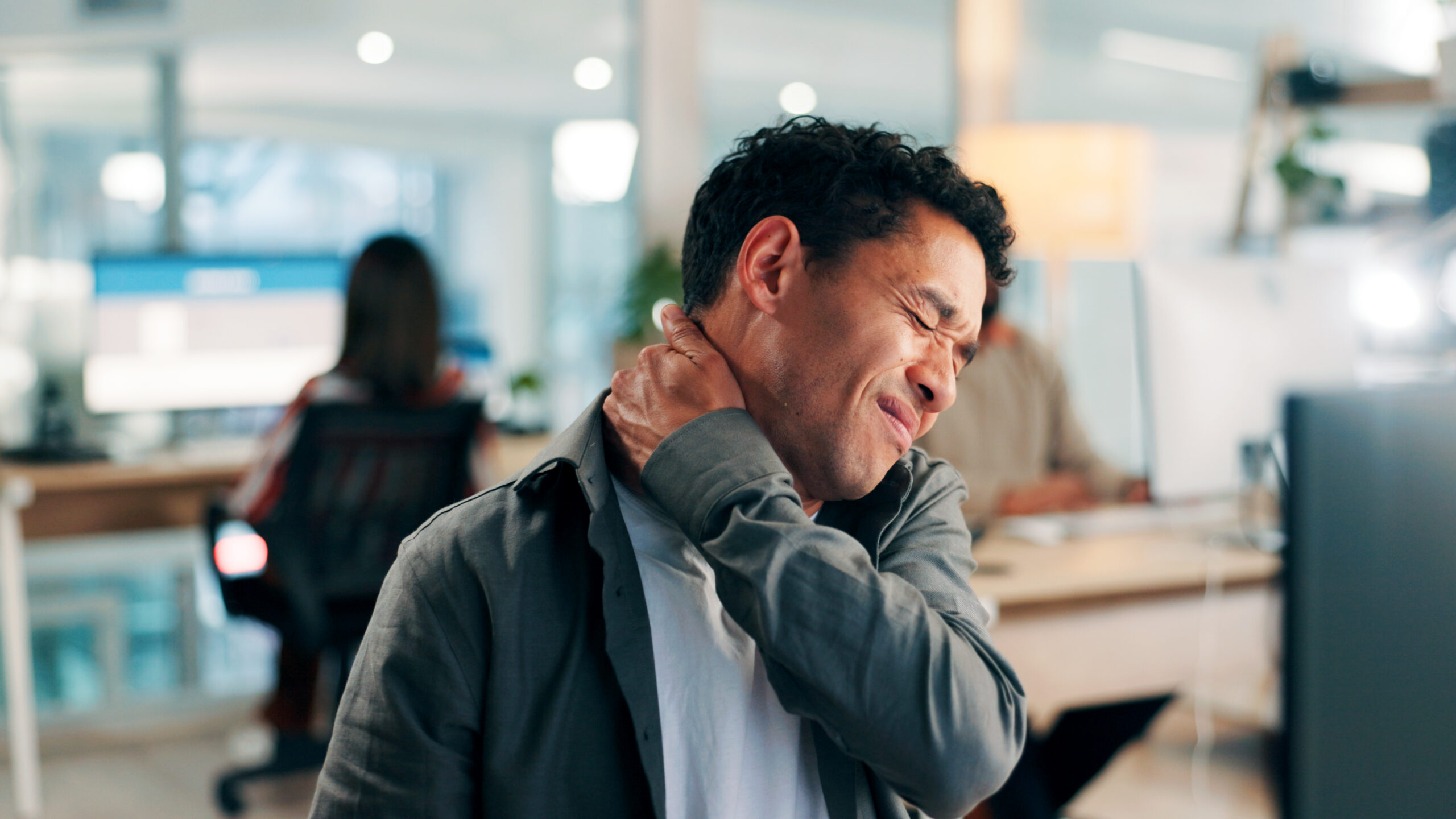 An office worker rubs his neck with a pained expression, highlighting neck pain from poor desk ergonomics.