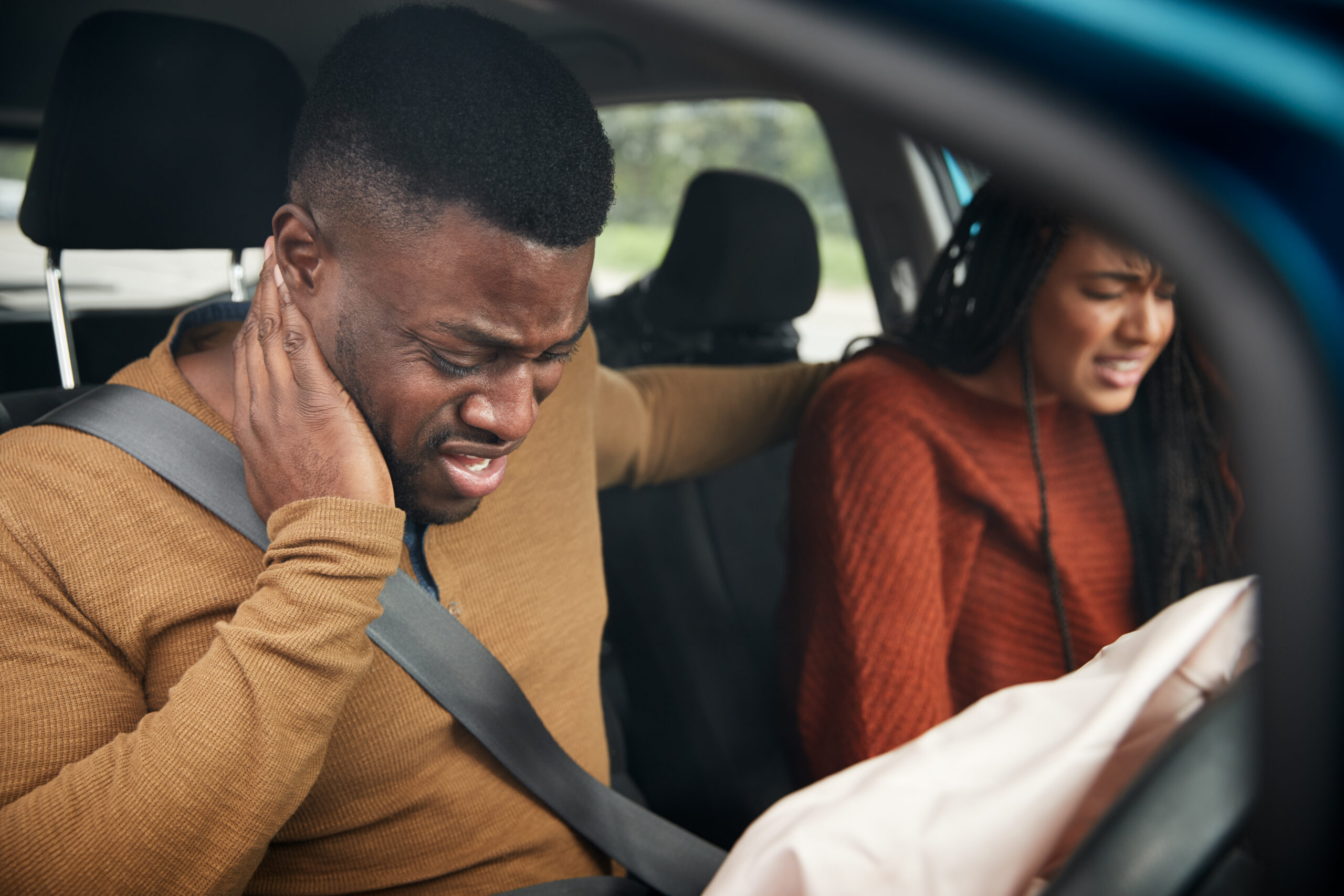 A man grips his neck in pain from whiplash inside a car with a deployed airbag after an accident.