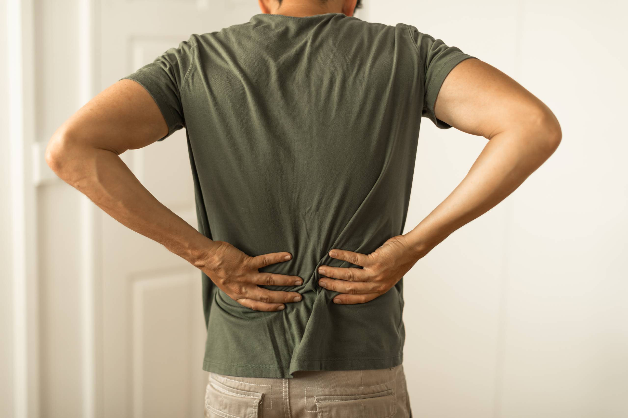 A man clutches his lower back in discomfort, illustrating chronic back pain or a muscle strain.