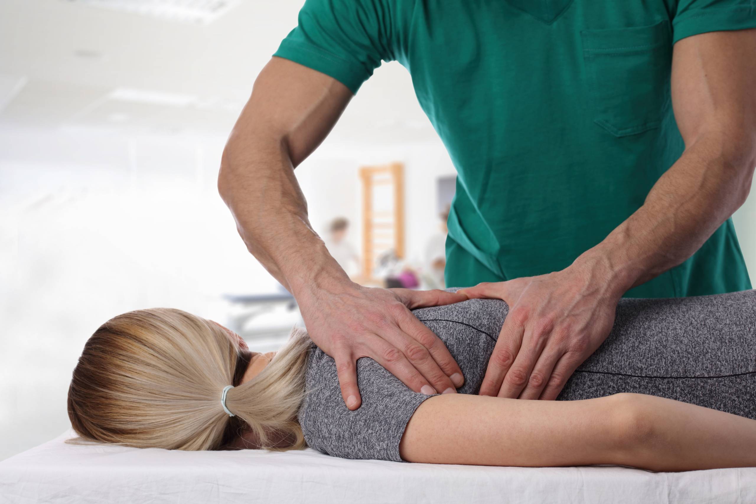 A practitioner in green scrubs performs a chiropractic adjustment on a patient lying face down.