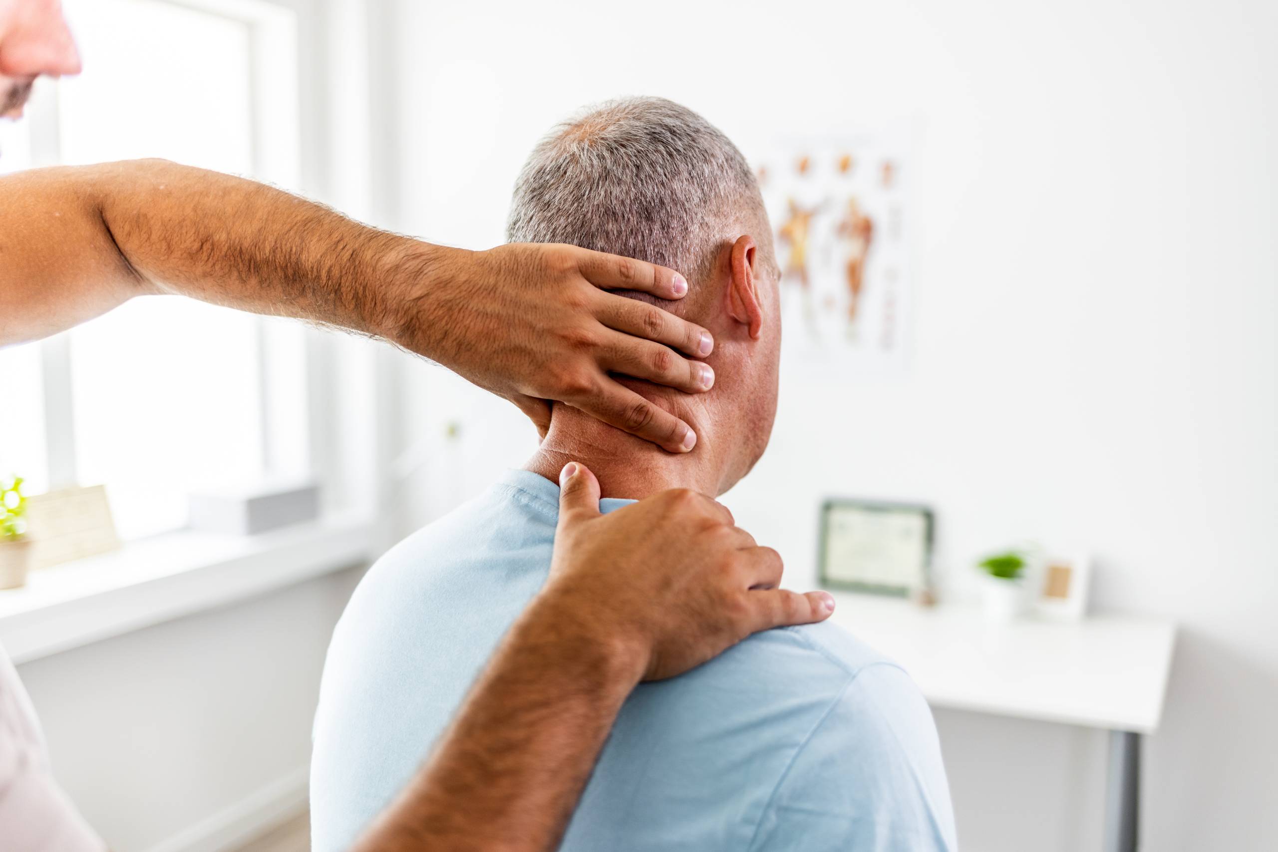 A practitioner conducts a chiropractic neck examination and spinal evaluation on a male patient.