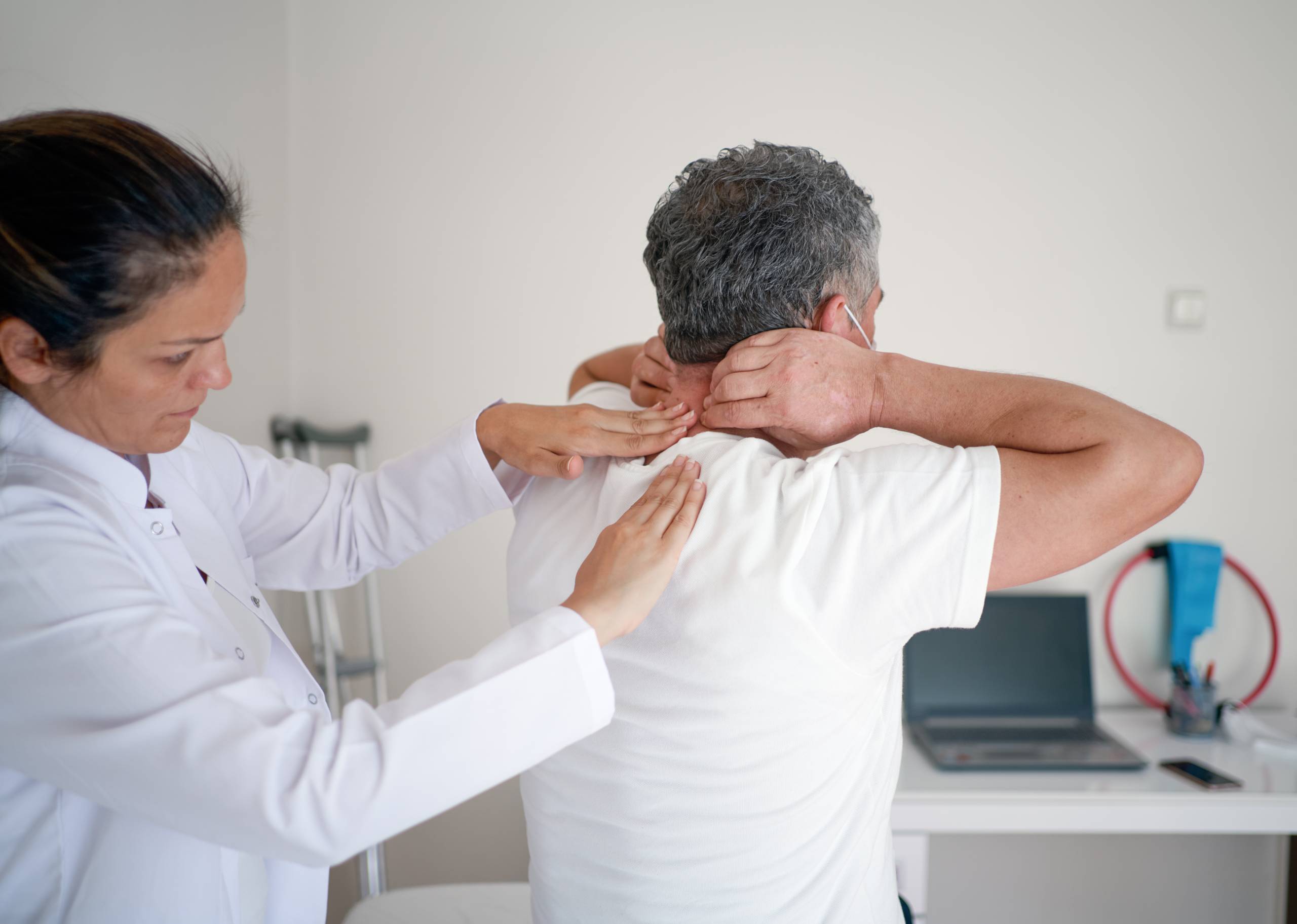 Chiropractor feeling for back pain on man’s back in chiropractic office setting.