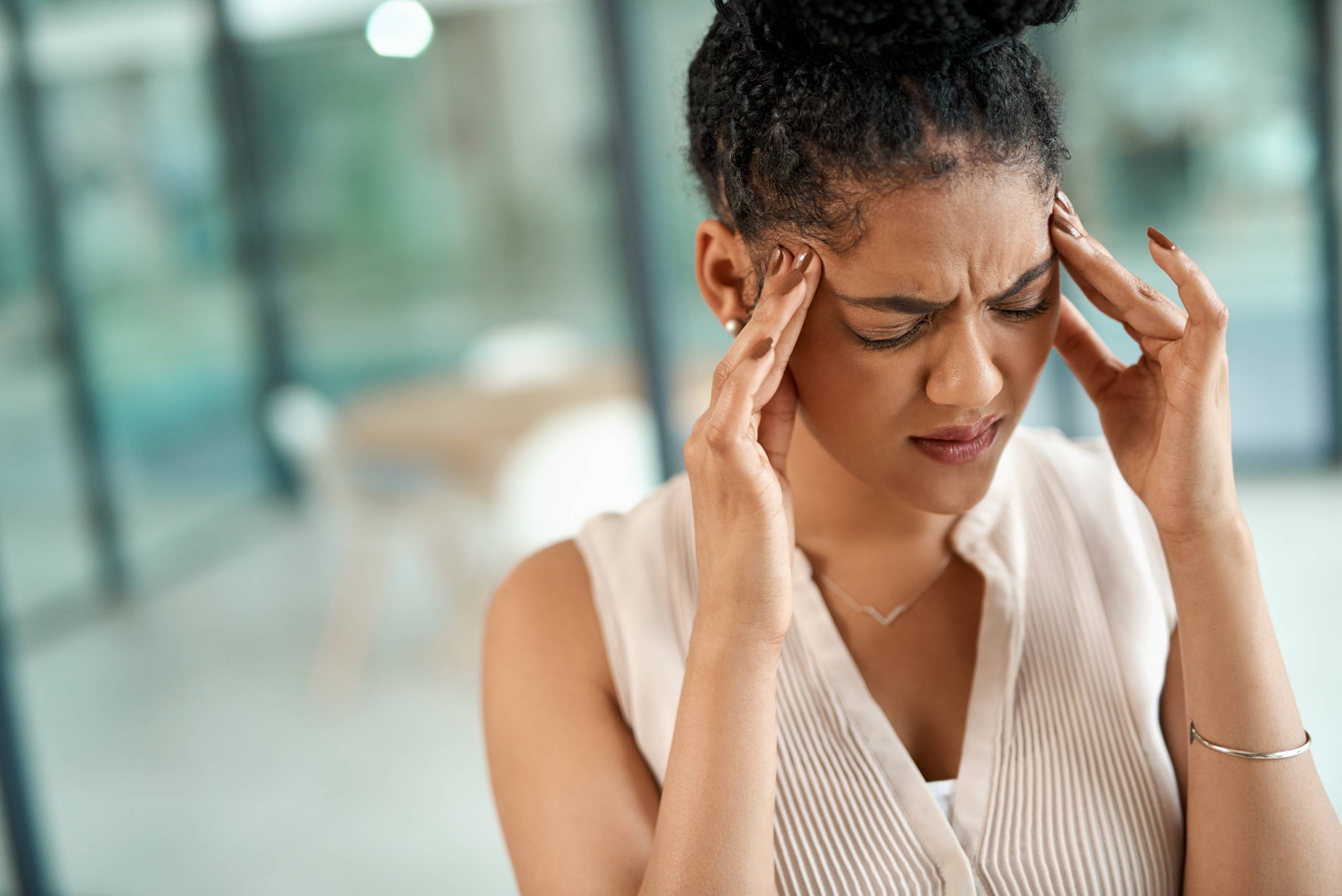 Woman holding both sides of forehead, signifying a migraine or headache pain.