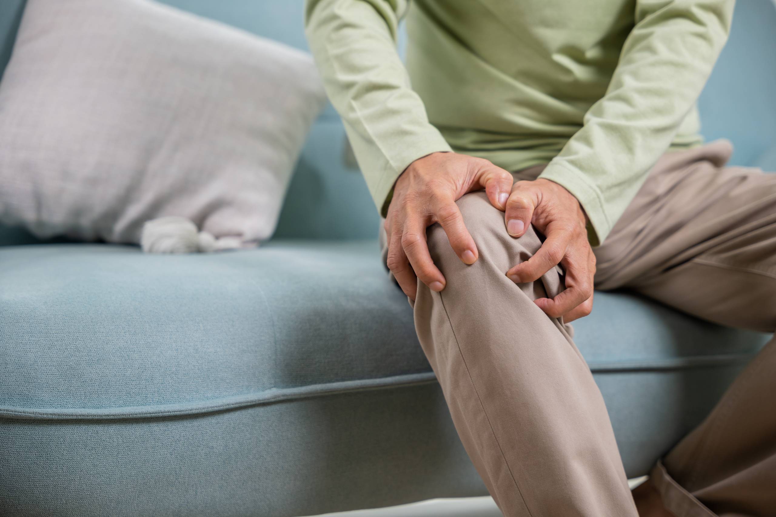 Man sitting on sofa holding his knee, signifying knee pain.