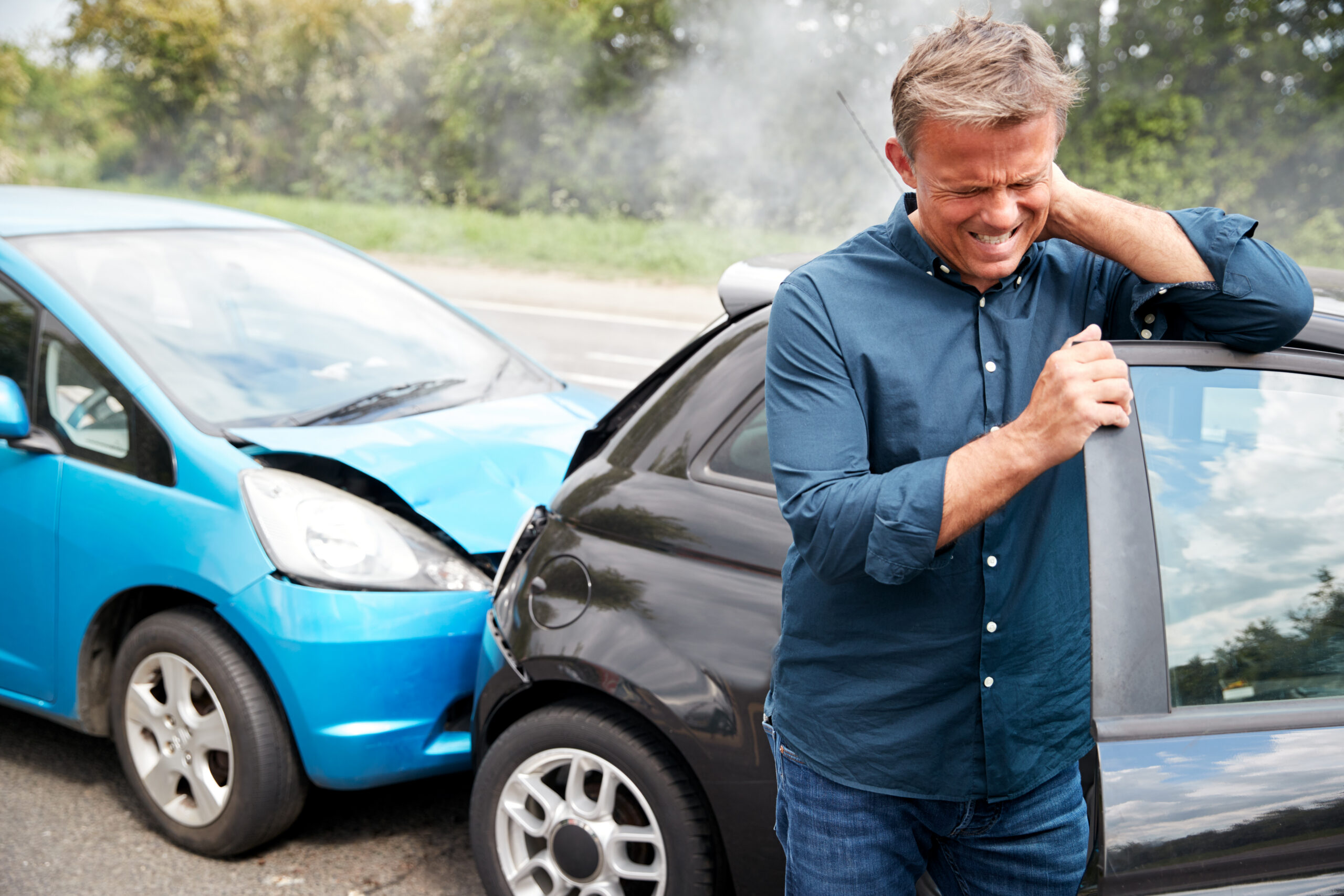 Man experiencing neck pain from whiplash while leaning on his car after a rear-end auto accident.